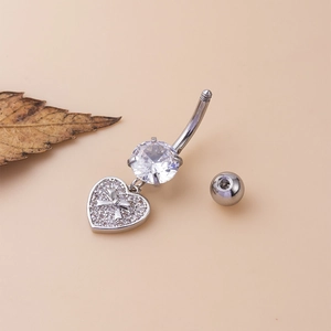 Piercing nombril argenté avec pendentif cœur papillon et zircons sur surface beige clair