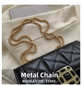 Detail shot of glossy black quilted bag with luxury gold chain and gemstone buckle