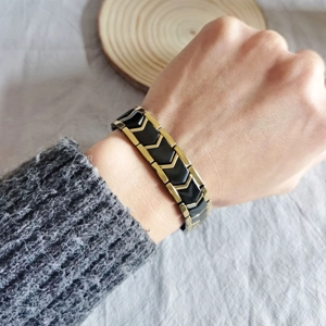 Macro detail of men's titanium bracelet featuring gold V-shapes and black magnetic links