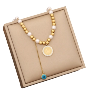 Gold coin pendant necklace with pearls, beads, and a blue evil eye charm on jewelry box