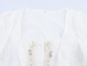 Close-up of white dress square neckline featuring 3D flowers, pearls, and sequins