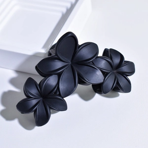Close-up of matte black flower hair claw clip with triple 3D floral design on white steps
