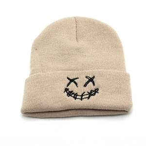 Detail view of khaki knit beanie featuring a black embroidered graffiti-style smiley face