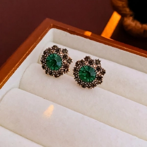 Gros plan détaillé des boucles d'oreilles strass vert émeraude avec monture dorée en boîte