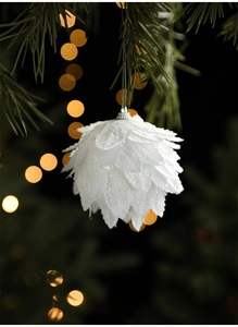 Close-up of white petal-shaped Christmas ball with glitter on pine tree branches