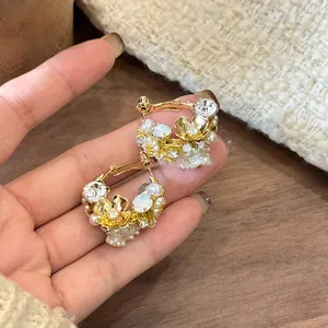 Macro shot of gold-plated flower earrings with pearls and crystals held in hand