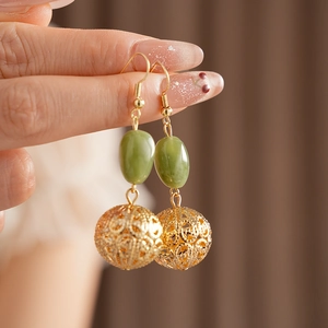 Detail of hand holding gold hook earring with green resin stone and hollow round pendant