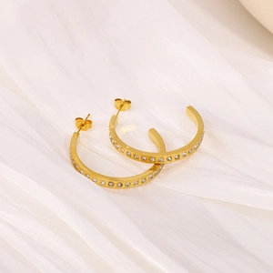 Boucles d'oreilles créoles dorées en C avec cristaux CZ sur tissu blanc doux