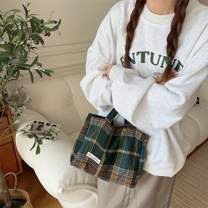 Detail of green plaid wool tote bag showing texture and woven label in lifestyle setting