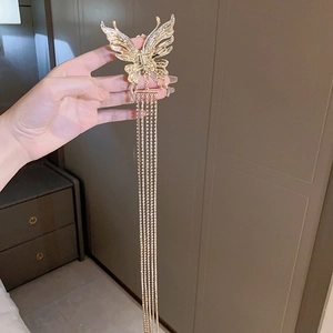 Détail d'une pince à cheveux papillon dorée avec de longs glands en strass tenue en main