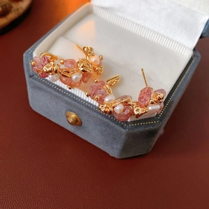 Detail of C-shaped gold earrings with strawberry quartz and pearls in a velvet jewelry box