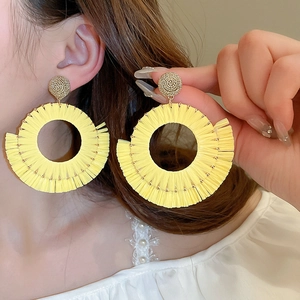 Detail of model wearing large yellow raffia fringe hoop earrings in a bohemian style
