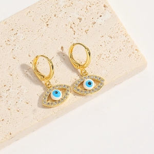 Detailed close-up of golden evil eye hoop earrings with blue stones on beige stone