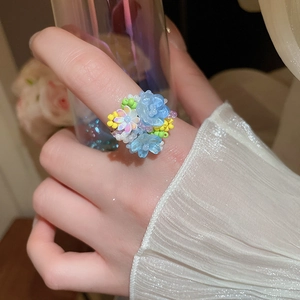 Dettaglio anello di fiori fatto a mano con petali azzurri e perle indossato al dito