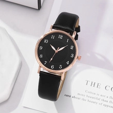 Minimalist quartz watch with rose gold case and black leather strap on decorative card