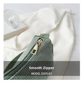 Detail of a smooth golden metal zipper on a green corduroy crossbody shoulder bag