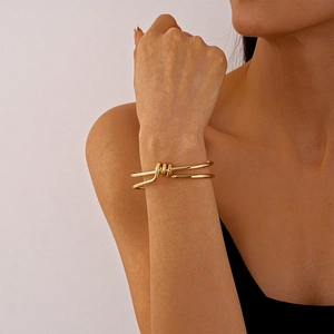Detailed view of the double-layered gold knot cuff bracelet on a woman wrist