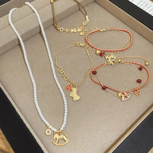 Detailed set of pearl necklace and bracelets with gold horse charms in a beige jewelry tray