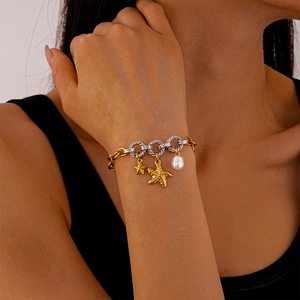 Close-up of beach style bracelet with gold starfish, pearl, and two-tone rings on wrist