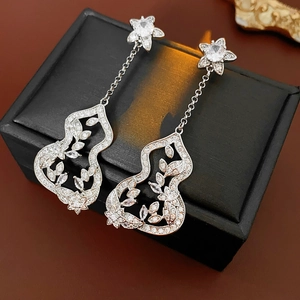 Detail of silver gourd-shaped earrings with floral cutouts and crystals on a jewelry box