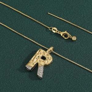 Macro shot of gold letter R pendant with white zircon stones on green leather background