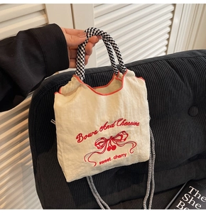 Detail of cream pleated fabric bag with embroidered cherry and woven checkered handle