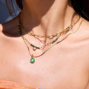 Close-up of layered gold necklaces with green natural stone and heart pendants on a model