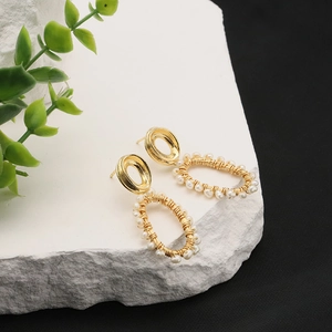 Elegant gold oval earrings with small white pearls on a textured white stone background