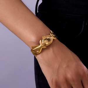 Detail view of a gold fish-shaped chain bracelet on wrist with matte metal finish