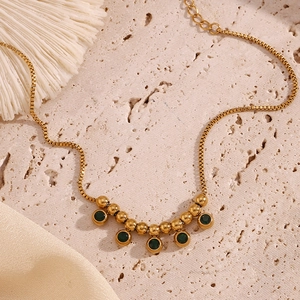 Detail of 18K gold plated steel anklet with green zircon beads on stone texture