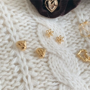 Flat lay of gold heart bow earrings and flower studs on a white knitted sweater background