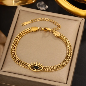 Macro view of gold stainless steel woven bracelet featuring a black evil eye charm