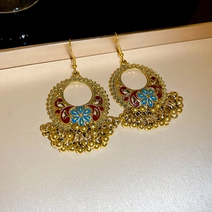 Detailed view of ethnic gold Jhumka earrings with blue enamel flowers and metal tassels