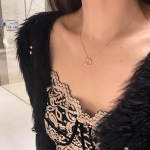 Close-up of a rose gold heart pendant necklace with white stones on a female model