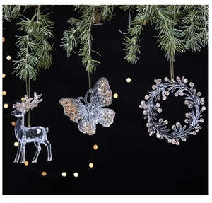 Close-up of clear acrylic reindeer and snowflake ornaments with gold sequins on pine branch