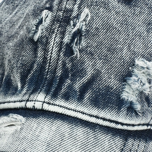 Detailed macro view of distressed blue denim baseball cap with heavy washed fabric textures