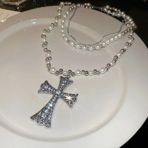 Close-up of a sparkling cross pendant necklace with pearls on white porcelain
