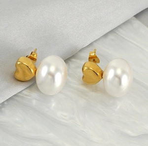 Detailansicht goldener Herz-Ohrstecker mit eleganten weißen Perlen auf Marmoruntergrund