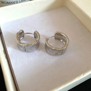 Detailed view of silver wide huggie earrings featuring zebra texture and beaded edges