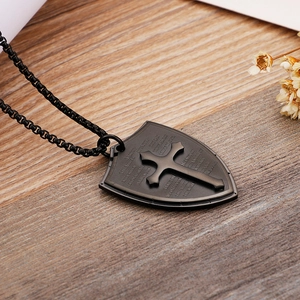 Macro detail of black shield cross pendant with engraved scripture on wood background