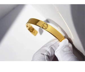 Close-up of gold plated snake chain bracelet with smiley face charm held in white glove