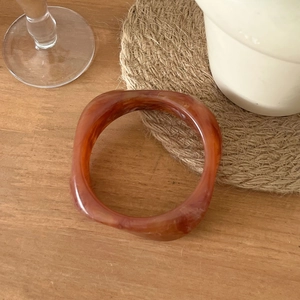 Bracelet large irrégulier en résine ambrée marbrée sur un décor de table en bois
