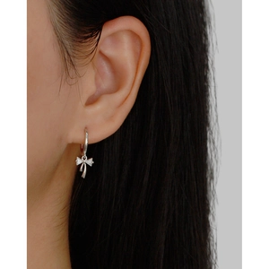 Detailed close-up of a silver bow earring with shimmering crystals on a model's ear