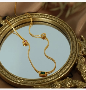 Detail of 18K gold snake chain with green zircon gemstones on vintage silk background