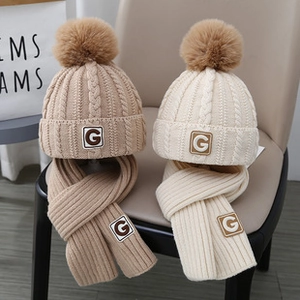 Dettaglio del set di cappelli e sciarpe in maglia con pompon e toppa con lettera G