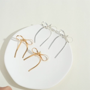 Elegant 14K gold and silver bow tassel earrings displayed on a white ceramic tray