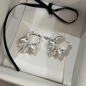 Detailed view of silver bow-shaped earrings inside a beige gift bag with jewelry branding
