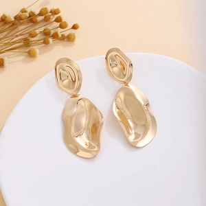 Detail view of irregular gold metallic wave earrings on a minimalist white platform