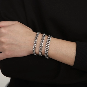 Close-up of three layered silver Cuban link bracelets in varying widths on a wrist