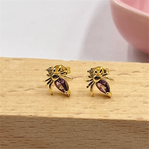 Macro shot of gold spider earrings with purple teardrop gemstones on a wood block